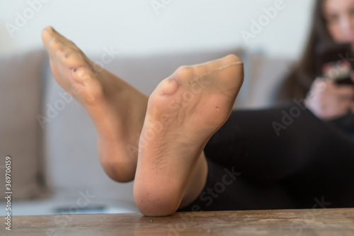 Lady at home sitting relaxing on the couch with feet on the table using her smartphone.  Focus on her soles, unfocused background.