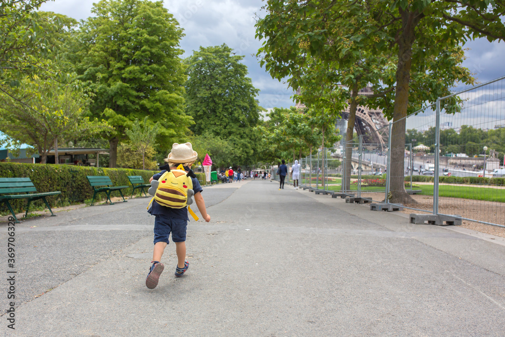 Happy blond toddler child, boy, visiting Paris during the summer, standing in front of the Eiffel tower