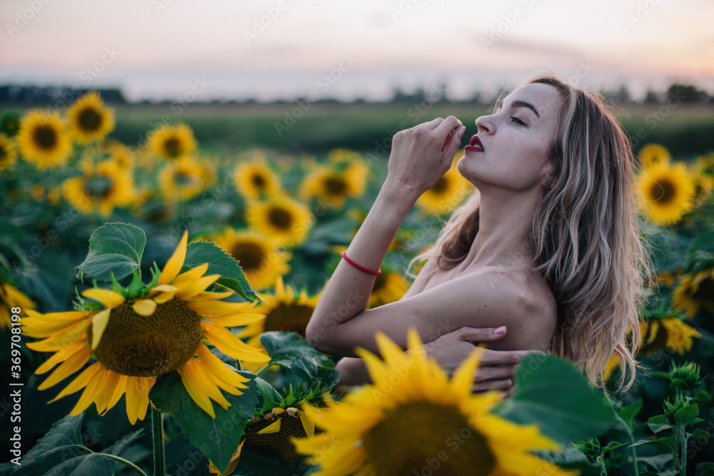 Young, slender girl topless poses at sunset in a field of sunflowers Young, slender girl topless poses at sunset in a field of sunflowers