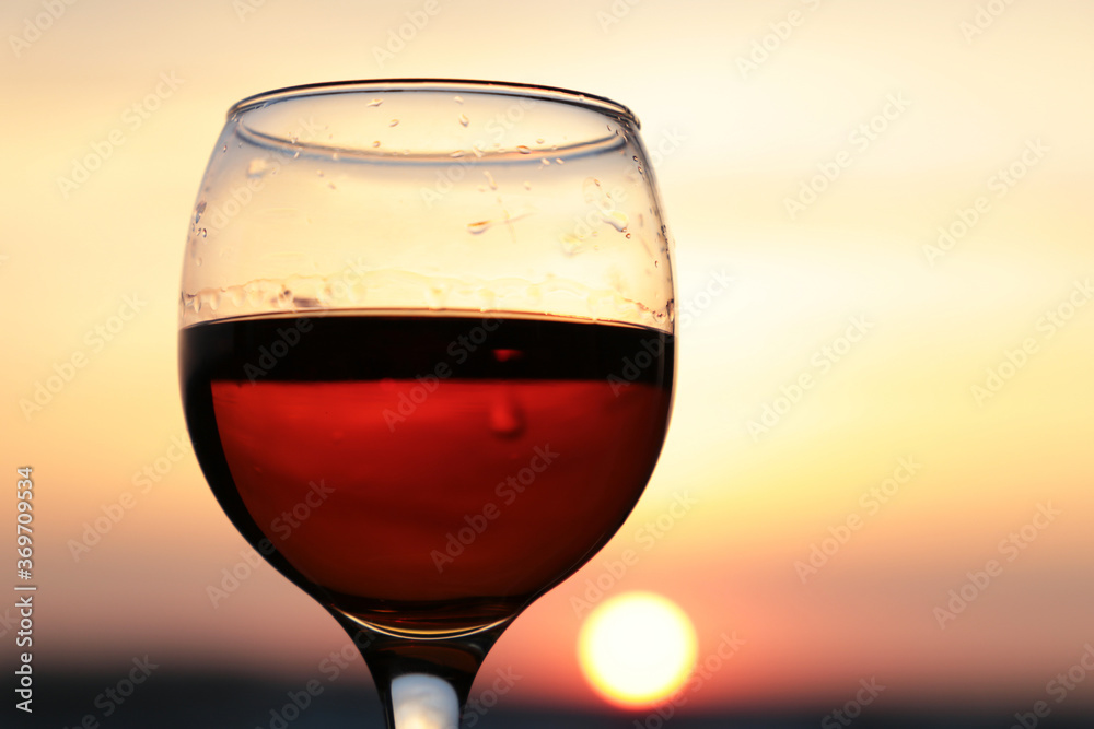 Glass of cognac on beautiful sunset background, sun and sky are reflected in alcohol drink. Concept of celebration, evening party at resort, romantic dinner outdoors