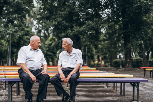 Two old senior adult men have a conversation outdoors in the city park.