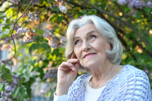 Senior beautiful woman posing with lilacs in park