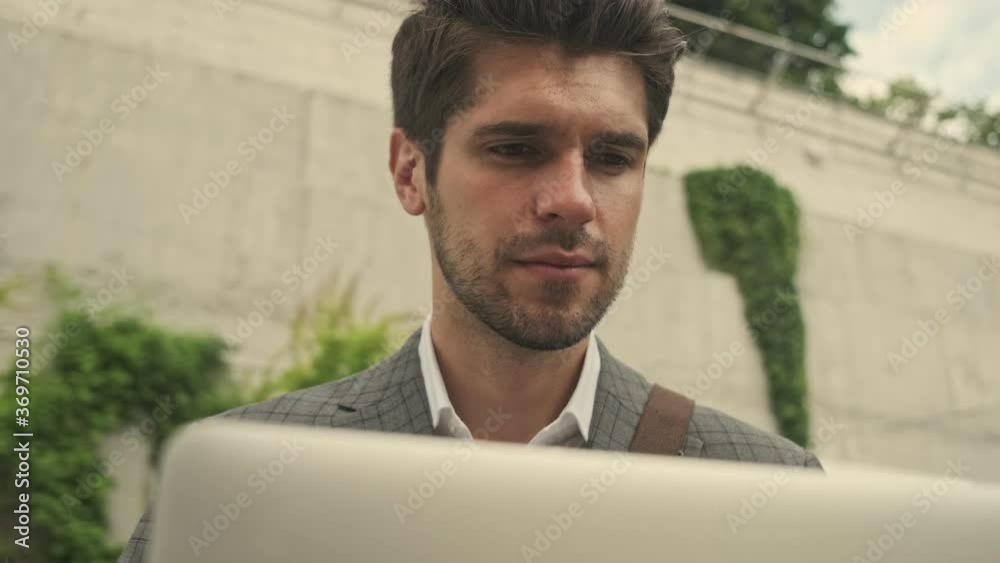 Focused handsome businessman using laptop computer while sitting on bench near the stairs outdoors