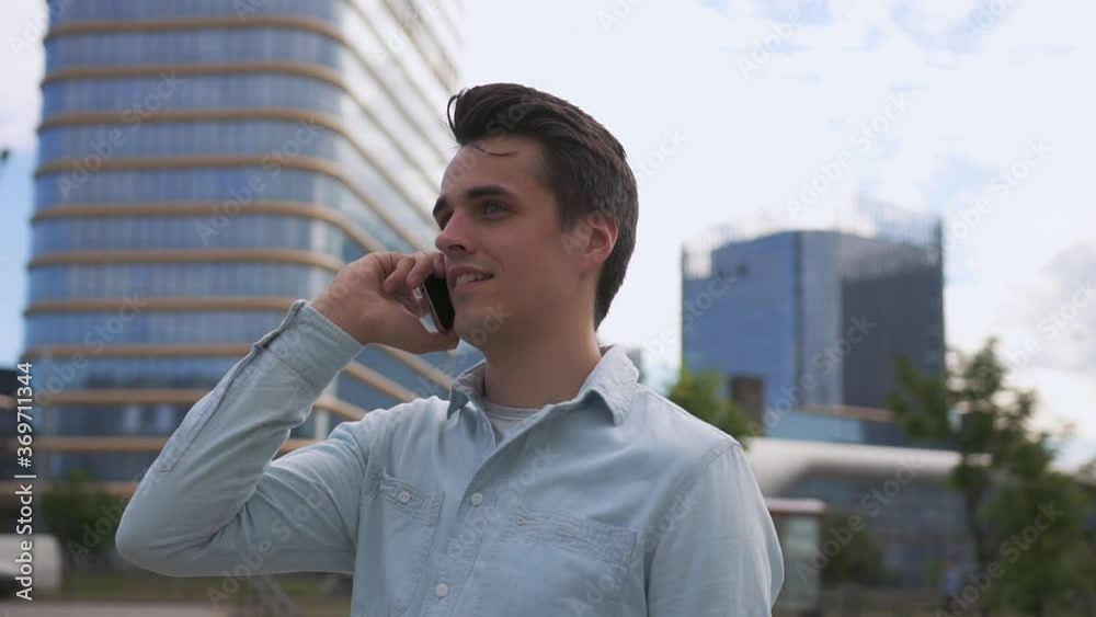 Panning slow motion shot of handsome young man speaks on the phone against the background of a modern city. Panning slow motion shot of handsome young man speaks on the phone against the background of a modern city.