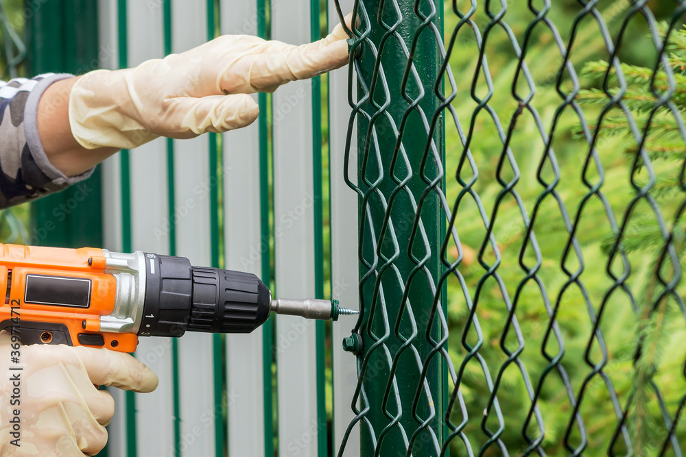 Work with a drill-screwdriver on a metal fence with a netting. Work with a drill-screwdriver on a metal fence with a netting.