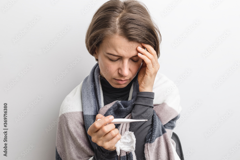 A sick woman with a cold looks at a temperature thermometer. A sick woman with a cold looks at a temperature thermometer.