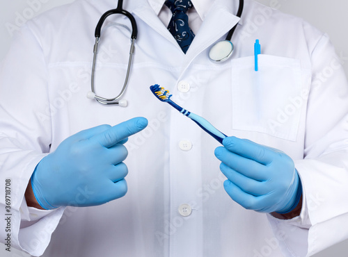 doctor therapist is dressed in a white robe uniform and blue sterile gloves is standing and holding a toothbrush