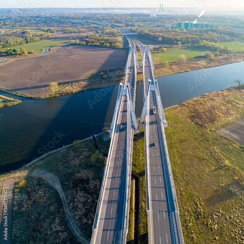 New modern double cable-stayed bridge with wide three-lane roads over Vistula River in Krakow, Poland. Part of the ring road around Krakow. Aerial view. Sedzimir Steelworks in the background