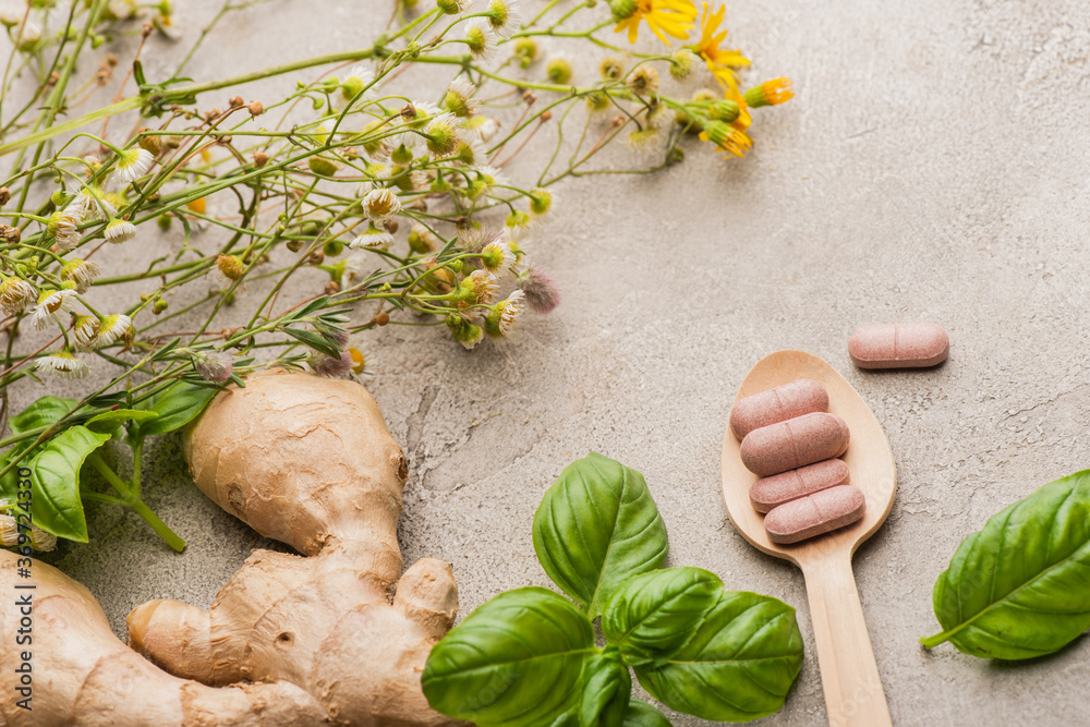 herb, green leaves, ginger root and pills in wooden spoon on concrete background, naturopathy concept herb, green leaves, ginger root and pills in wooden spoon on concrete background, naturopathy concept