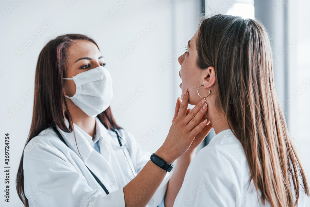Checking lymph nodes and throat. Young woman have a visit with female doctor in modern clinic Checking lymph nodes and throat. Young woman have a visit with female doctor in modern clinic