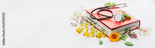 panoramic shot of herbs in book with stethoscope on white background, naturopathy concept