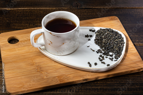 loose tea in a saucer next to a mug on a wooden background with different lighting