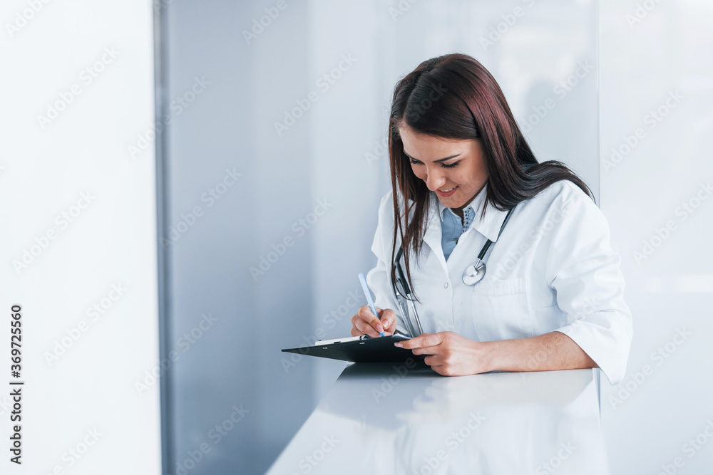 With notepad. Young nurse indoors in modern clinic. Conception of healthcare With notepad. Young nurse indoors in modern clinic. Conception of healthcare