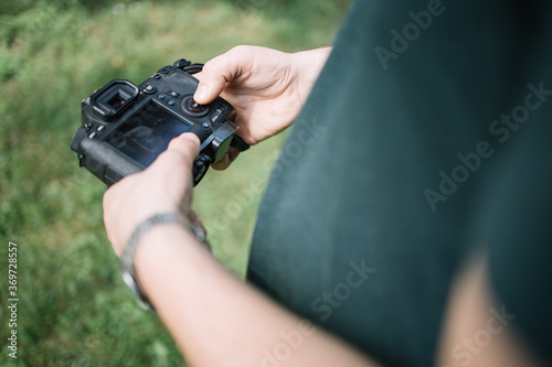 Close-up view of man hands holding camera and checking pictures. Cropped man holding professional camera and checking photos with grass in background.