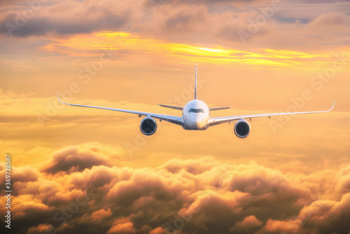 Commercial passenger aircraft flying above dramatic clouds in colourful sunset sky background. Transportation or travel concept.