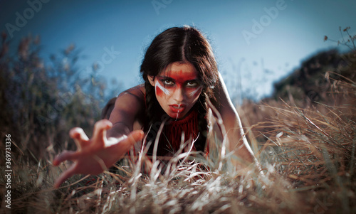 red-skinned Indian girl with red makeup on her face posing in yellow grass photo