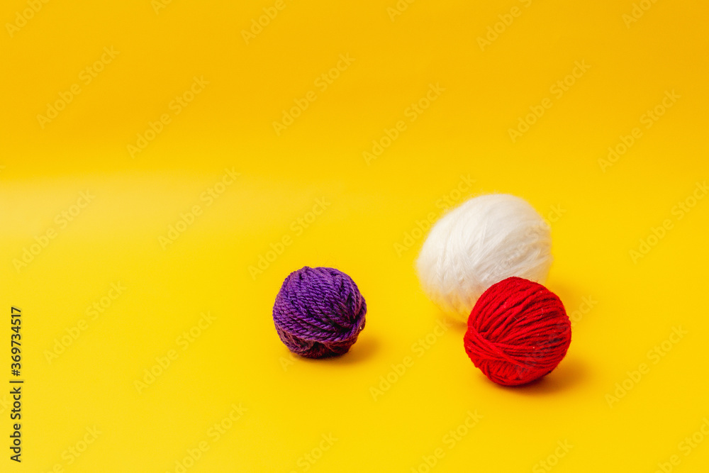 white, red and blue balls of wool lie on a yellow background white, red and blue balls of wool lie on a yellow background
