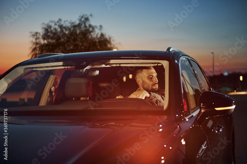 Handsome unshaved man in fashionable clothes riding his automobile