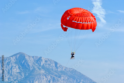 Tandem, two persons flying on a red parachute on sky background photo