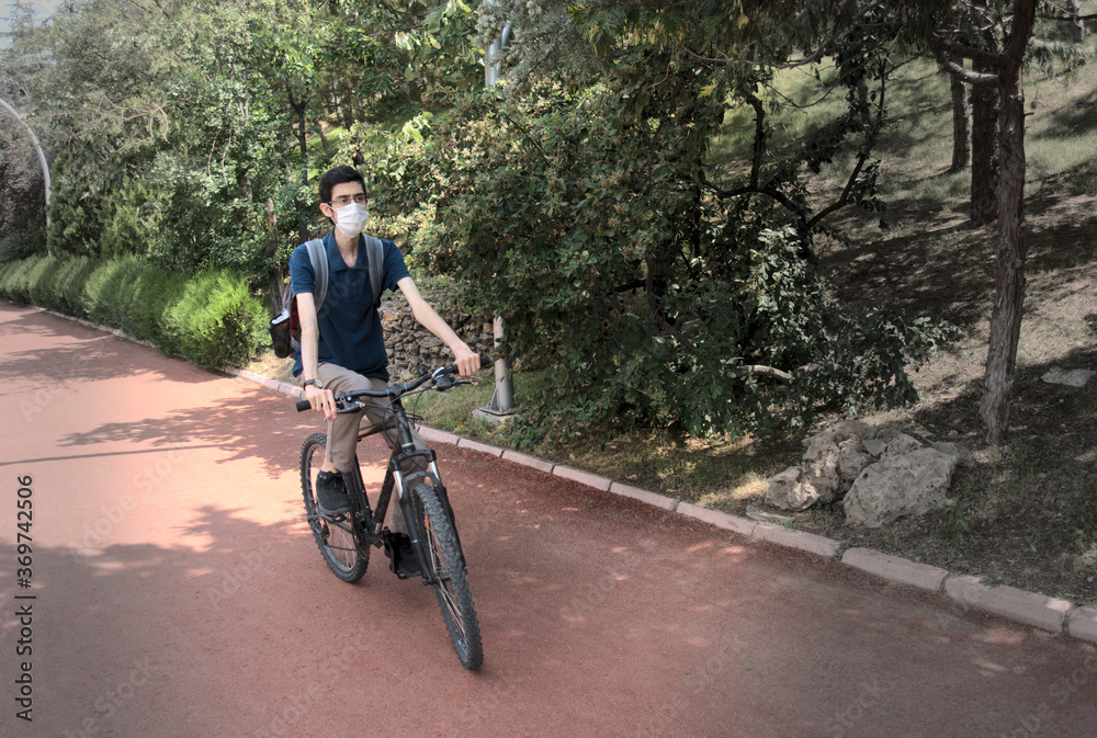 Obraz premium Isolated, skinny young male wearing a mask cycling on a bicycle path at a park