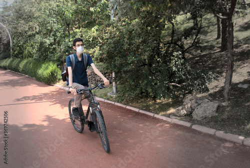 Isolated, skinny young male wearing a mask cycling on a bicycle path at a park