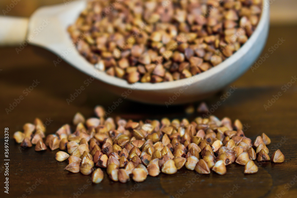 Buckwheat in a wooden spoon on a brown wooden background. Healthy food concept, vegetarian food. Diet foods. Copy space. Wooden spoon with buckwheat on a wooden table. Selective focus of 