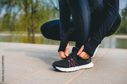 closeup view of woman's hands in sport suit tying up shoelaces on her sport sneakers while running in the park