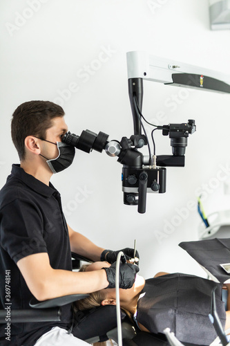 Male dentist examining senior woman looking on the teeth with professional microscope in dental office