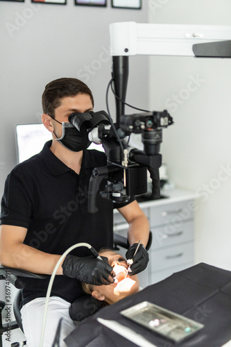 Dentist checking up patient teeth at dental clinic office. Microscope, professional dental treatment