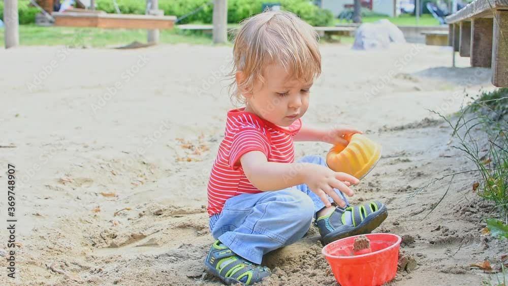 Cute little child having fun playing with sand and colorful toys in the park, beautiful summer sunny day in children playground Cute little child having fun playing with sand and colorful toys in the park, beautiful summer sunny day in children playground