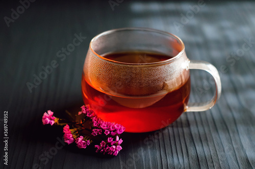 black tea in a transparent Cup next to a purple flower on a dark wooden background