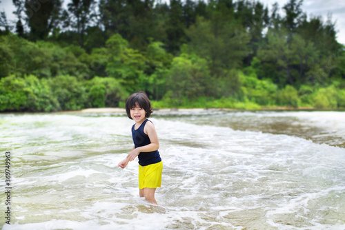 Fototapeta Naklejka Na Ścianę i Meble -  Cute Asian boy standing in the waves by the sea.Child having fun outdoor.Wildschooling young male playing in the water at the shore.