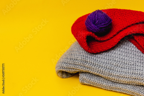 on an orange background is a gray folded sweater and a red scarf, there are red and blue balls of woolen thread