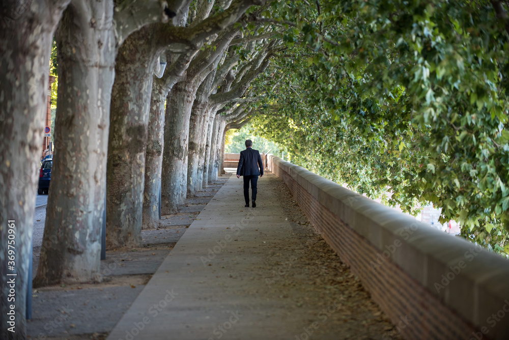 homme marchant seul dans une ville sous une allée d'arbres 