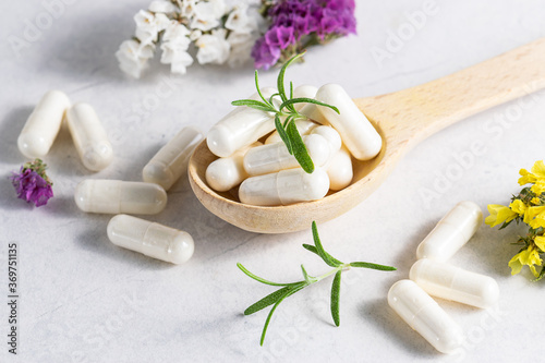Fototapeta Naklejka Na Ścianę i Meble -  Collagen capsules for skin and beauty in the wooden spoon with herbs and flowers on white marble table close up. Health care concept.