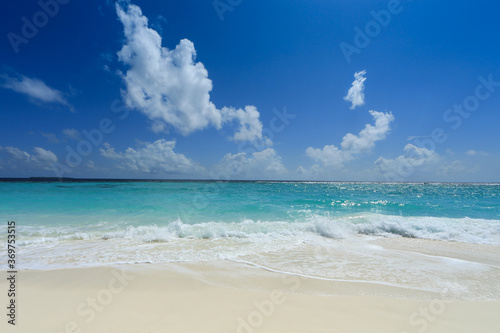 Bright white sand and gentle ocean waves under deep blue cloudy sky of Maldives.