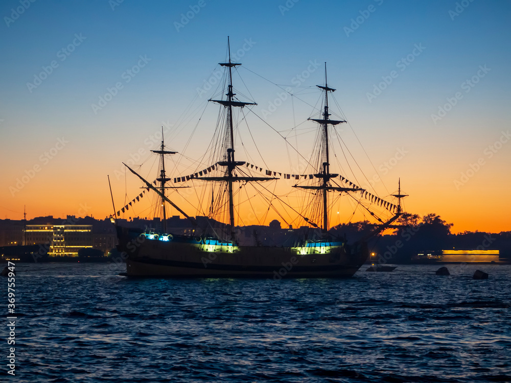 an old sailing frigate in the waters of the Neva river against the background of the Peter and Paul fortress at sunset