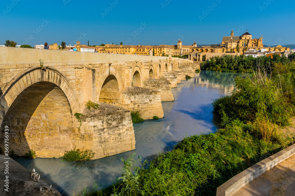 A view across the Guadalquivir river and the Roman bridge leading into the ancient city of Cordoba, Spain in the summertime