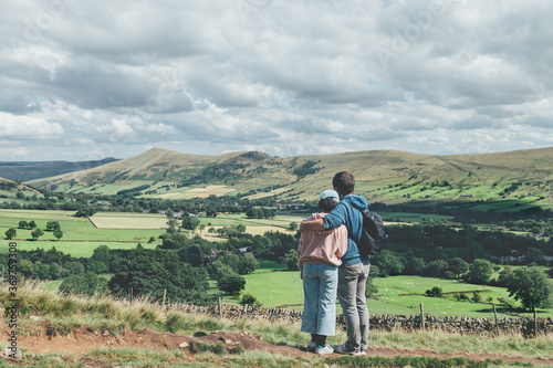 Father is hugging his daughter and they areobserving beautiful field view on Edale village and Mam Tor at Peak District National Park, England, UK while hiking. Staycation concept of traveling local