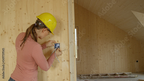 CLOSE UP: Young female electrician screws an outlet frame onto a wooden wall