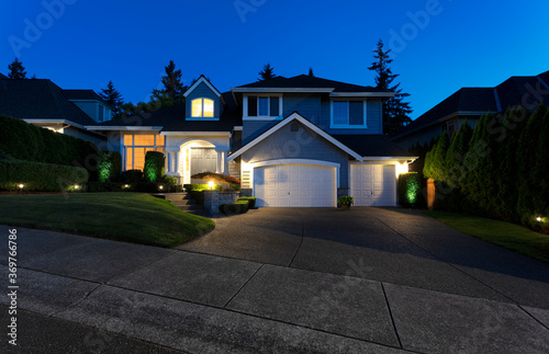 Suburban home exterior on a summer late evening with lights on yard and house