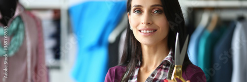 Portrait of beautiful smiling dressmaker holding scissors. Creative and talented seamstress working in fashion studio. Copy space in left side. Small atelier business concept © H_Ko