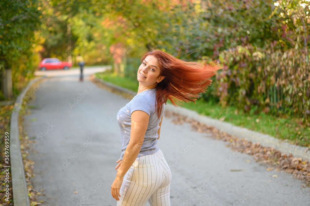 A beautiful red-haired woman walks in the park on a warm autumn day. The girl turns around. A beautiful red-haired woman walks in the park on a warm autumn day. The girl turns around.