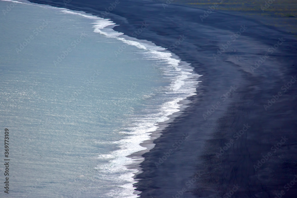 Waves of the Atlantic ocean fall on the black sand of the beach of Iceland from a height
