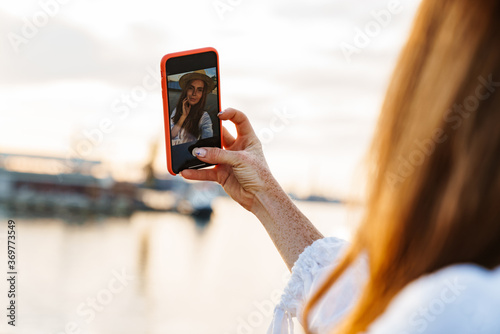 Image of happy ginger woman smiling and taking selfie on mobile phone