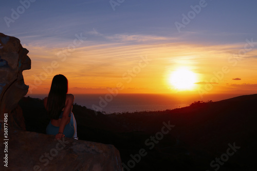 silhouette of a fit woman girl on the top of a rock mountain top overlooking a sunset ocean view 