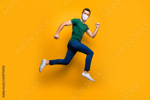 Full length body size view of his he attractive sporty healthy guy wearing safety n95 mask jumping running marathon stop mers cov influenza pandemia isolated vibrant yellow color background