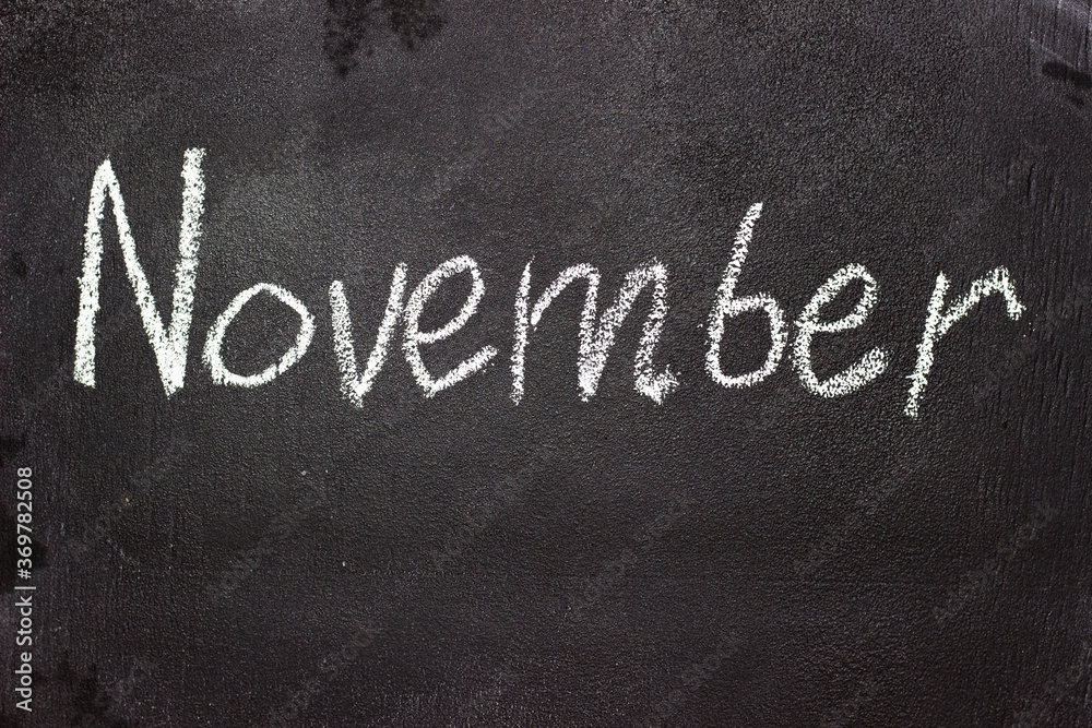 Fototapeta premium Month written in white chalk on a chalkboard. The month depicted on the chalkboard is November