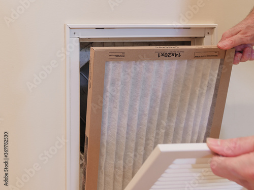 HVAC service technician replacing dirty indoor air filter in residential heating and air conditioning system. Home air duct ventilation system maintenance for clean air. 