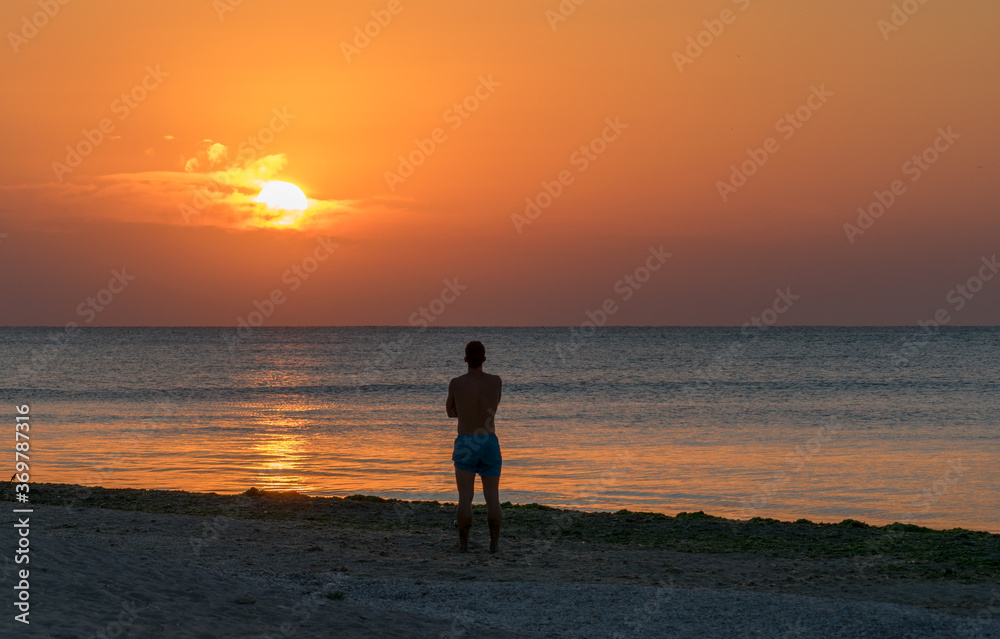 The man sits alone on the beach and admires the sunrise. Meditation, relaxation
